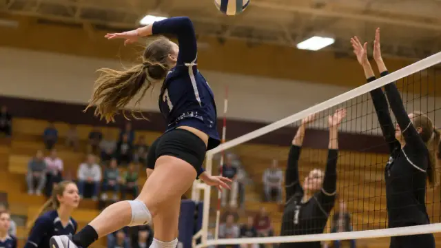 High school volleyball player jumping to spike the ball in a gym
